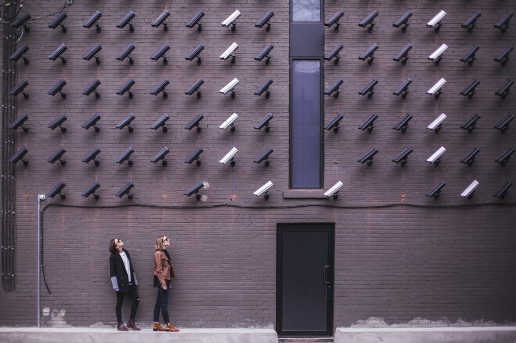 The Art of Drawing Readers In: Your attractive post title goes here Women observing a wall covered with numerous security cameras in an urban setting, showcasing modern surveillance.